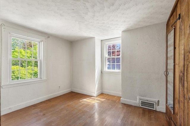 spare room with baseboards, hardwood / wood-style floors, plenty of natural light, and a textured ceiling