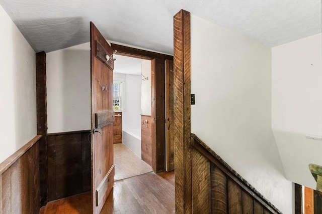 hall with wood finished floors and a wainscoted wall