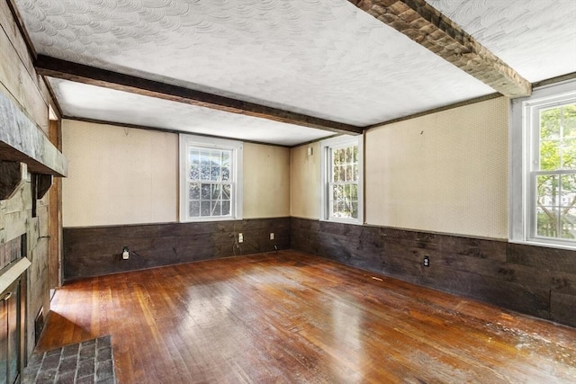 empty room with wood-type flooring, beamed ceiling, wood walls, wainscoting, and a fireplace with flush hearth