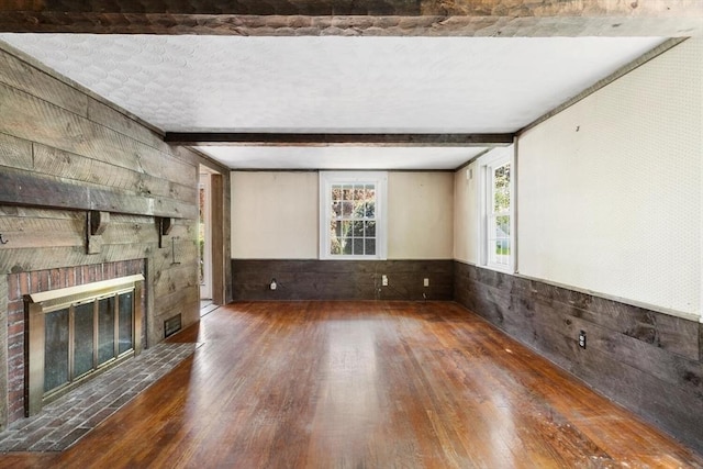 unfurnished living room with wood finished floors, wood walls, beam ceiling, a fireplace, and a wainscoted wall