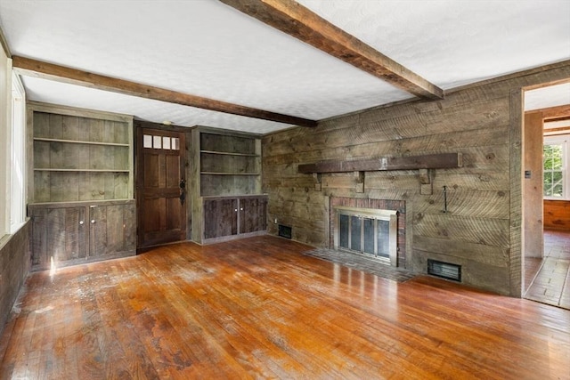 unfurnished living room with a large fireplace, wood-type flooring, beam ceiling, wood walls, and built in features