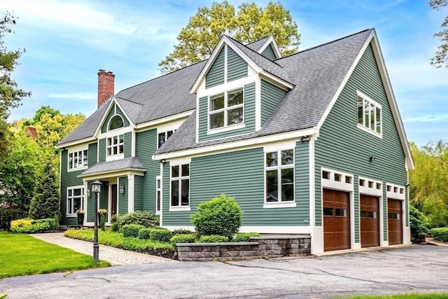 view of front of house with roof with shingles, a garage, a chimney, and driveway