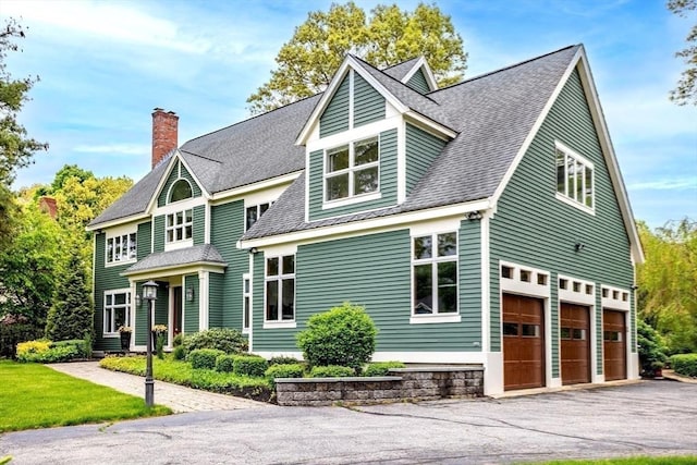 view of front of property featuring an attached garage, a chimney, and driveway