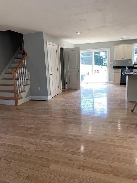 unfurnished living room with stairs, recessed lighting, baseboards, and light wood-style flooring