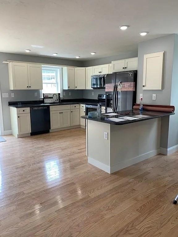 kitchen featuring dark countertops, baseboards, black appliances, and light wood finished floors