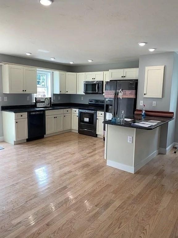 kitchen with dark countertops, baseboards, black appliances, and light wood-type flooring