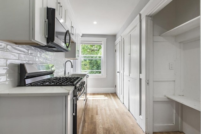 39 Pond St, Framingham, MA 01702 - kitchen featuring stainless steel appliances, light wood-style floors, tasteful backsplash, baseboards, and white cabinetry