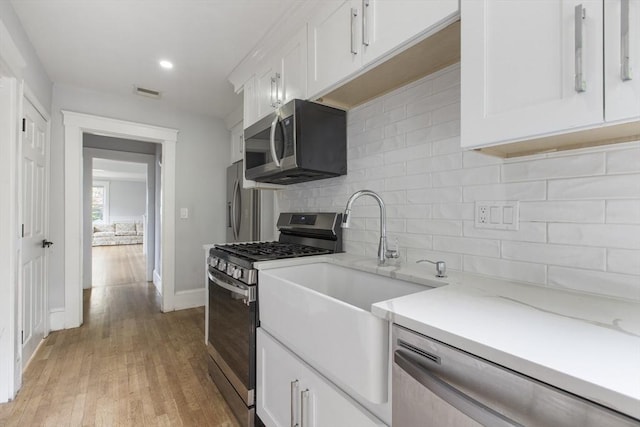 39 Pond St, Framingham, MA 01702 - kitchen with stainless steel appliances, white cabinets, backsplash, baseboards, and light wood finished floors