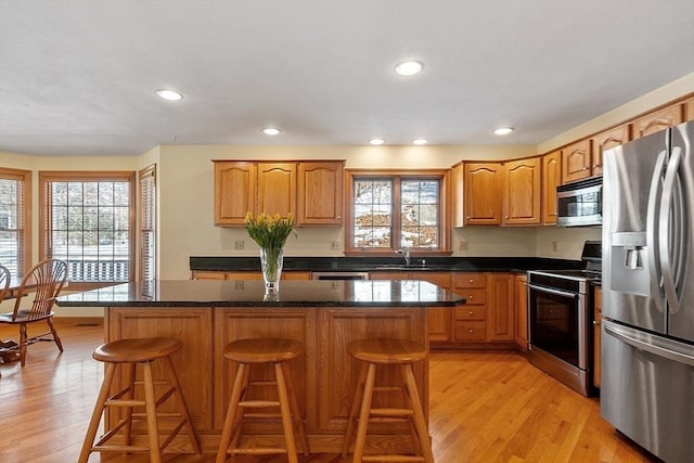 kitchen with appliances with stainless steel finishes, a center island, light wood-style floors, a kitchen bar, and a sink