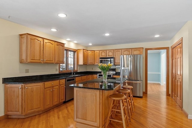 kitchen with a center island, recessed lighting, appliances with stainless steel finishes, dark stone countertops, and light wood-type flooring