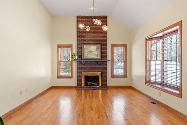 unfurnished living room with lofted ceiling, a brick fireplace, baseboards, and wood finished floors