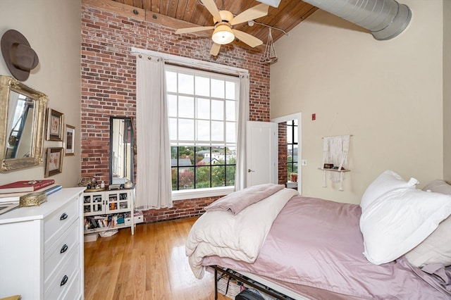 bedroom with brick wall, high vaulted ceiling, wooden ceiling, ceiling fan, and light hardwood / wood-style flooring