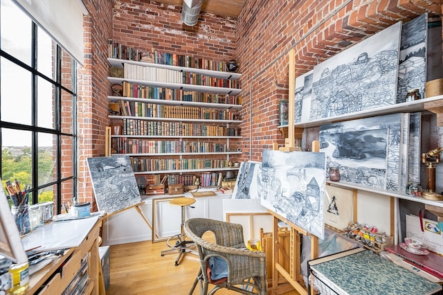 sitting room with a towering ceiling, light hardwood / wood-style flooring, and brick wall