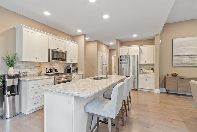 kitchen with a sink, stainless steel appliances, light wood finished floors, backsplash, and a kitchen breakfast bar