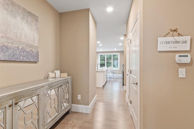 corridor with a sink, light wood-style flooring, recessed lighting, and baseboards