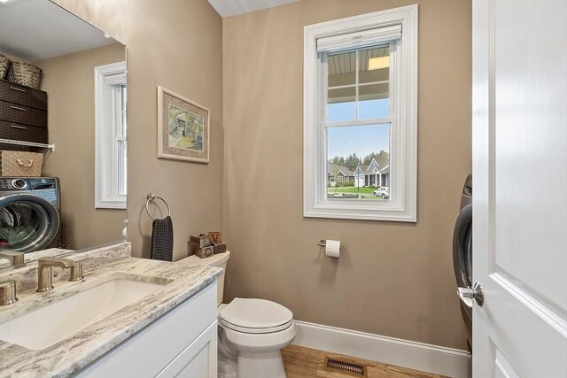 half bathroom with washer / clothes dryer, toilet, baseboards, vanity, and wood finished floors