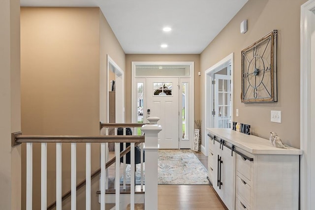 corridor with light wood finished floors, recessed lighting, and an upstairs landing