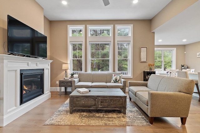 living area with wood finished floors, a glass covered fireplace, recessed lighting, and baseboards