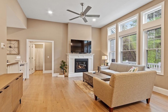 living room featuring ceiling fan, light wood-style floors, baseboards, a glass covered fireplace, and recessed lighting