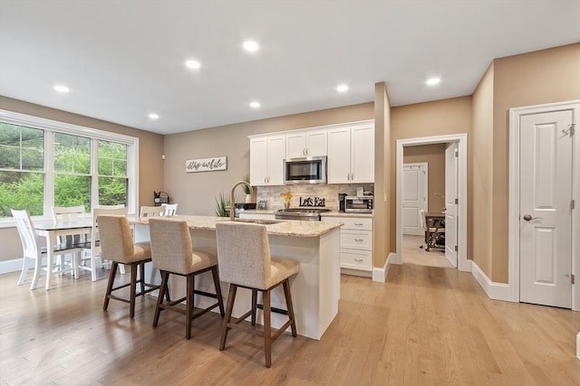 kitchen with stainless steel microwave, a center island with sink, a breakfast bar area, a sink, and tasteful backsplash