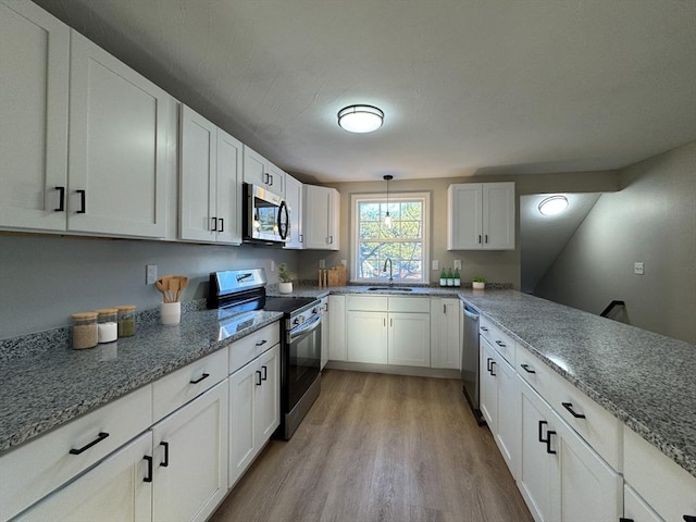 kitchen featuring white cabinetry, sink, stainless steel appliances, pendant lighting, and light hardwood / wood-style floors