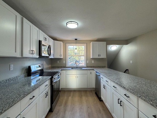 kitchen with white cabinets, hanging light fixtures, sink, light hardwood / wood-style flooring, and appliances with stainless steel finishes