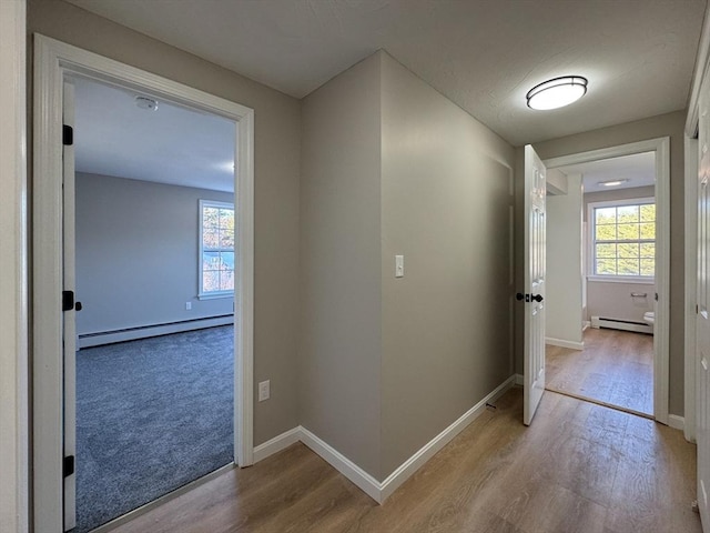 hall with baseboard heating and light hardwood / wood-style flooring