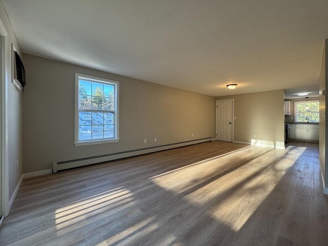 empty room featuring sink, plenty of natural light, wood-type flooring, and a baseboard heating unit