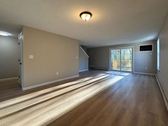 unfurnished living room featuring wood-type flooring and a baseboard heating unit