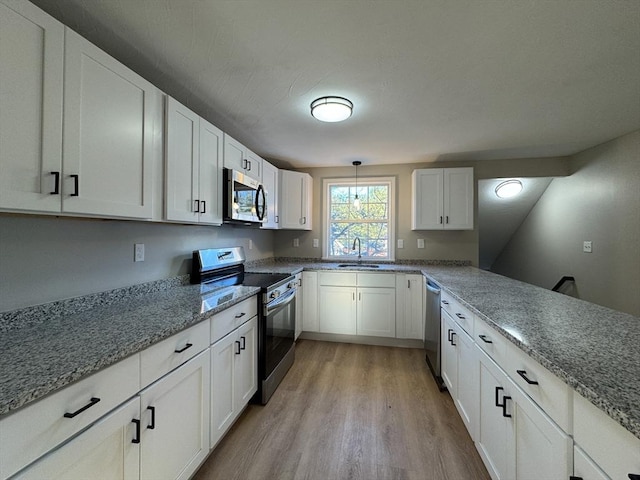 kitchen featuring white cabinets, hanging light fixtures, sink, appliances with stainless steel finishes, and light hardwood / wood-style floors