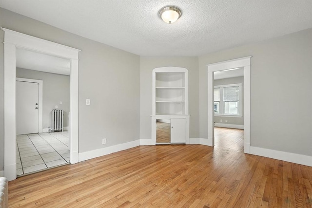 31-33 Dorset St, Springfield, MA 01108 - empty room featuring radiator heating unit, light wood finished floors, a textured ceiling, and built in shelves