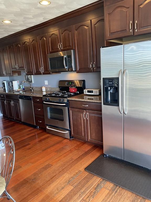 kitchen featuring dark brown cabinetry, sink, wood-type flooring, stone counters, and stainless steel appliances