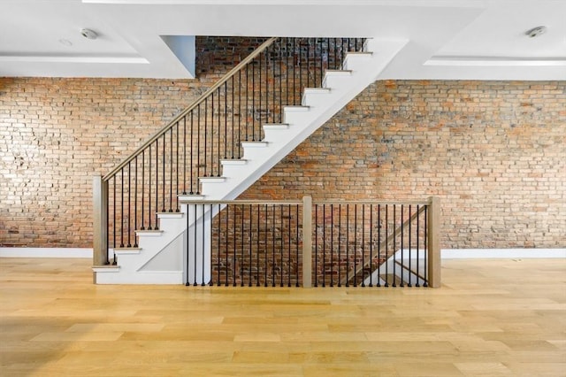 stairway with baseboards, a tray ceiling, wood finished floors, and brick wall