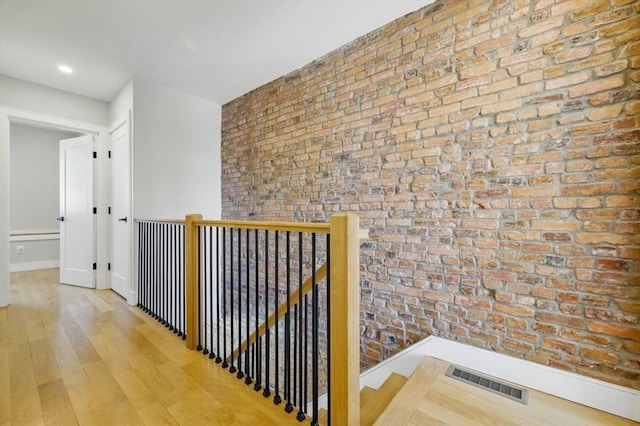 hallway featuring visible vents, wood finished floors, brick wall, and an upstairs landing