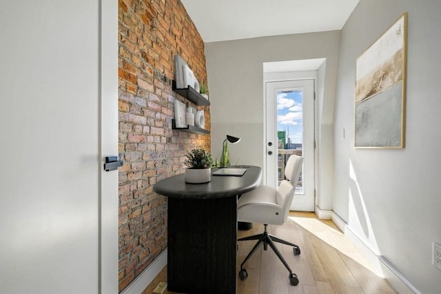 office area with light wood-style floors, baseboards, and brick wall
