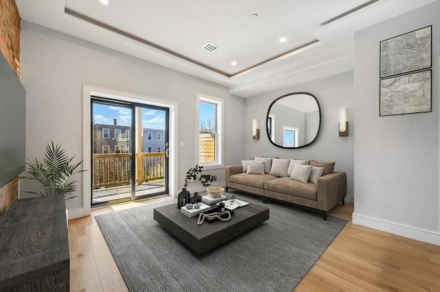 living room with visible vents, light wood-style floors, baseboards, recessed lighting, and a raised ceiling