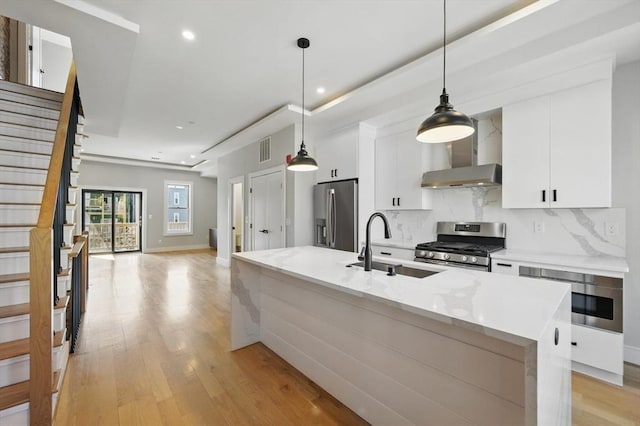 kitchen featuring wall chimney range hood, visible vents, a sink, white cabinets, and stainless steel appliances