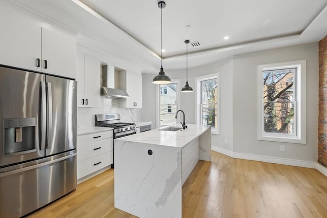 kitchen with wall chimney range hood, a sink, a raised ceiling, stainless steel appliances, and baseboards