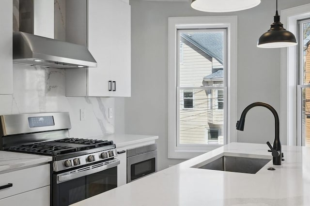 kitchen featuring wall chimney range hood, appliances with stainless steel finishes, a sink, white cabinetry, and decorative backsplash