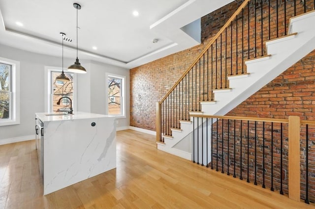 interior space featuring brick wall, light wood-type flooring, a sink, baseboards, and a raised ceiling