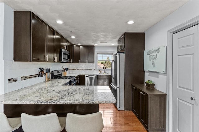12 School St Unit 3, Salem, MA 01970 - kitchen with appliances with stainless steel finishes, dark brown cabinets, a peninsula, light wood finished floors, and tasteful backsplash