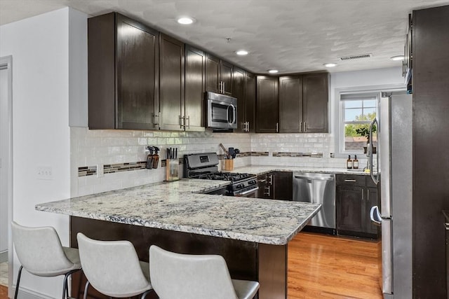 12 School St Unit 3, Salem, MA 01970 - kitchen with appliances with stainless steel finishes, a peninsula, dark brown cabinetry, decorative backsplash, and recessed lighting
