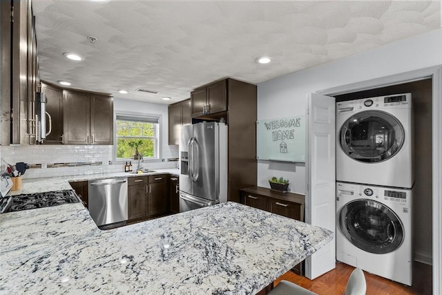 12 School St Unit 3, Salem, MA 01970 - kitchen featuring stainless steel appliances, stacked washer / drying machine, dark brown cabinets, light stone counters, and decorative backsplash