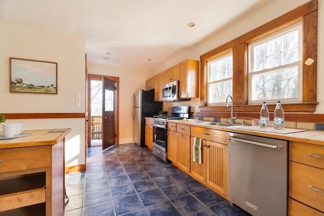 kitchen with tile counters, a wealth of natural light, appliances with stainless steel finishes, and sink