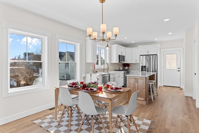 dining space with sink, a notable chandelier, and light wood-type flooring