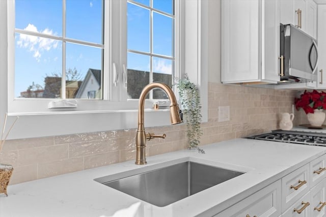 kitchen featuring backsplash, sink, appliances with stainless steel finishes, light stone counters, and white cabinetry