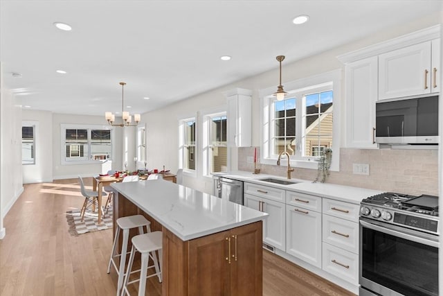 kitchen featuring hanging light fixtures, light wood-type flooring, a kitchen island, white cabinetry, and stainless steel appliances