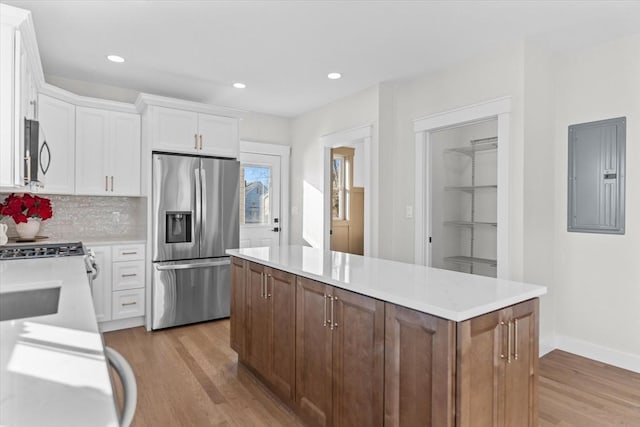 kitchen featuring stainless steel appliances, light hardwood / wood-style flooring, backsplash, electric panel, and white cabinets