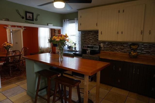 kitchen featuring stainless steel range with electric stovetop, light tile patterned floors, ceiling fan, cream cabinetry, and backsplash