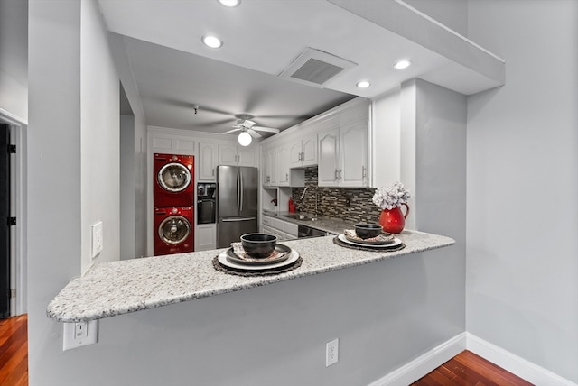 kitchen with kitchen peninsula, dark hardwood / wood-style floors, white cabinetry, stacked washer / drying machine, and stainless steel refrigerator